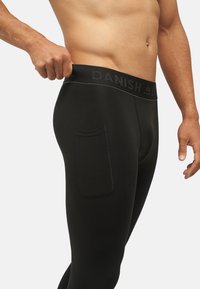 Zwarte leggings met een aansluitend ontwerp, gemaakt van rekbare stof. Heeft een brede tailleband met de tekst "DANISH" en een zijzak op de dij.