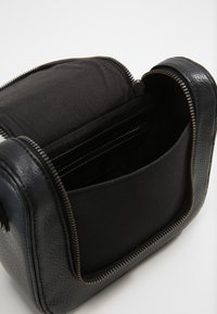 Borsa in pelle nera con superficie testurizzata, chiusura con zip e scomparti interni in tessuto nero. Mostra dettagli di cucitura lungo la zip.
