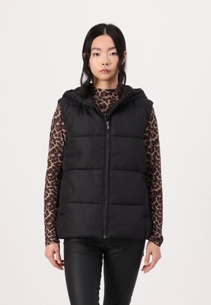 Vest negru căptușit cu glugă, dotat cu închidere cu fermoar și matlasare. Purtați peste un top cu mânecă lungă cu imprimeu leopard, asortat cu pantaloni negri.