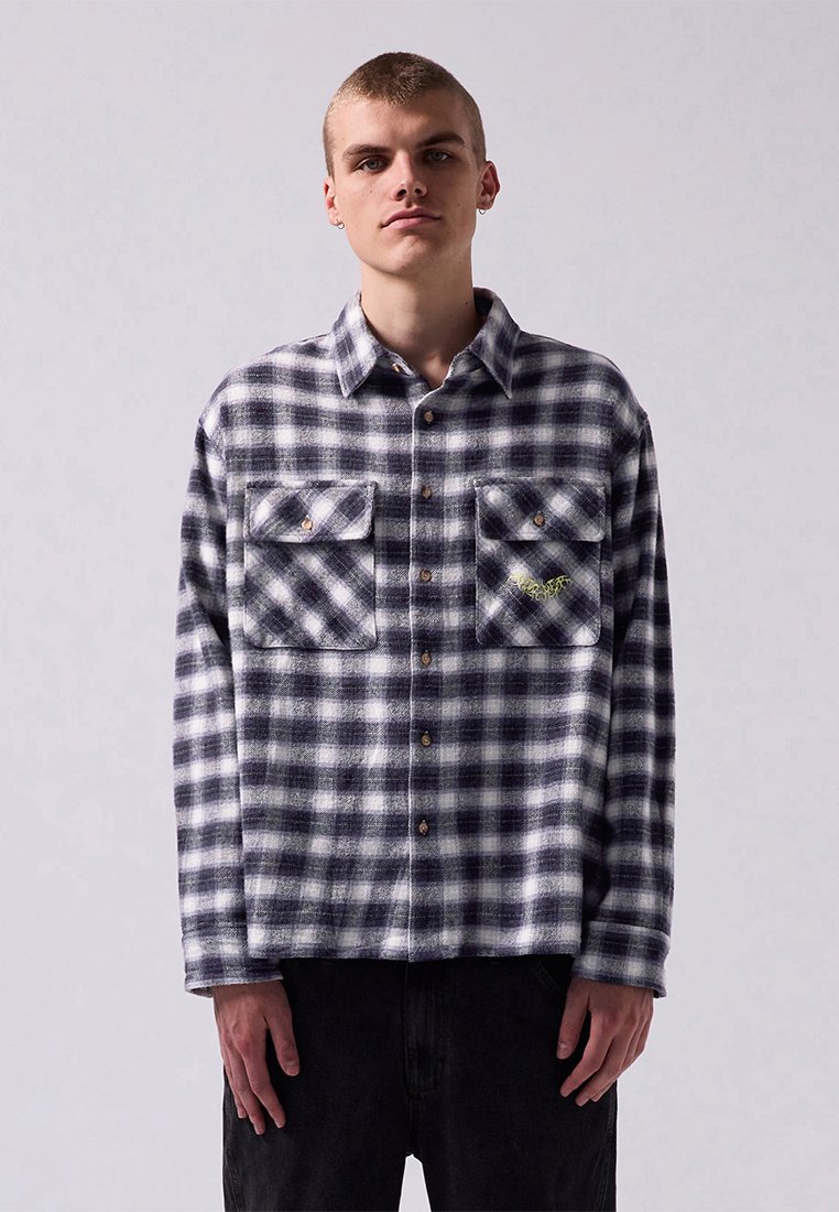 Plaid flannel shirt in navy and white, featuring two chest pockets with button closures and an embroidered detail. Soft texture, relaxed fit.