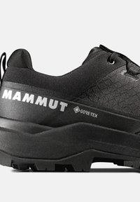 Schwarzer Mammut Gore-Tex Wanderschuh mit dicker Sohle, strukturiertem Obermaterial, Schnürung und Zuglasche an der Ferse, seitlich dargestellt.