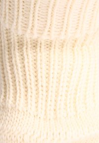Sciarpa lavorata a maglia di colore crema con un motivo testurizzato a coste, che mette in mostra un filato spesso e morbido e un design robusto.