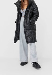 Zwarte pufferjas met een glanzende afwerking, oversized ontwerp en grote capuchon. Draag een grijze wijde broek en chunky zwarte plateau schoenen.
