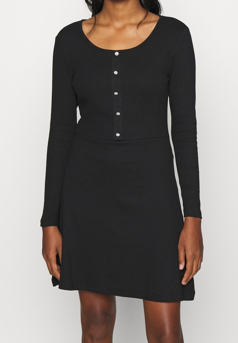 Svart långärmad klänning med rundad halsringning, med en knappslå och en figursydd överdel som fladdrar lätt vid fållen.