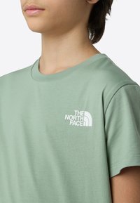 Világoszöld pamut póló kerek nyakkivágással és rövid ujjakkal. Bal mellrészen egy kis fehér logó található.