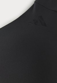 Crni atletski tekstil s glatkom teksturom i elegantnim krojem. Uključuje teksturirani, suptilno integrirani logo u crnoj boji.