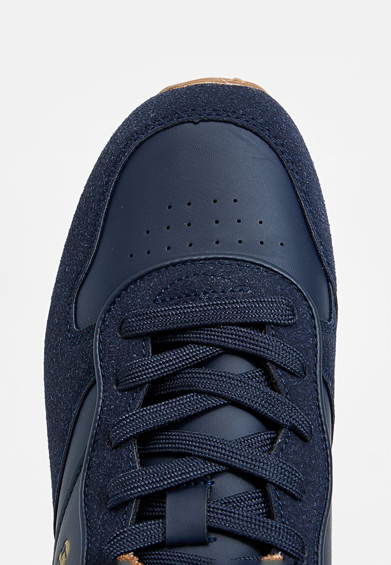 Granatowe trampki z teksturowanej zamszowej i gładkiej skórzanej cholewki, z wiązaniem i perforowanym detalem na palcach. Złoty akcent na logo.