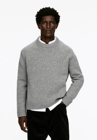 Grauer gestrickter Pullover mit einem runden Ausschnitt, gerippten Bündchen und Saum. Über einem weißen Hemd mit Kragen getragen, mit lässiger Passform und weicher Textur.