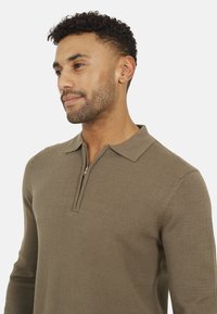 Maglione khaki con zip al collo, realizzato in tessuto a maglia, caratterizzato da un colletto strutturato, maniche lunghe e orlo a costine. Design semplice con linee pulite.