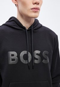 Μαύρο φούτερ με κουκούλα και ματ λογότυπο "BOSS" σε γκρι χρώμα. Διαθέτει ρυθμιζόμενα κορδόνια και απαλό, υφασμάτινο ύφασμα με υφή.