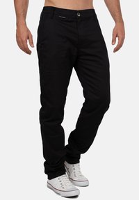 Pantaloni neri in cotone con taglio dritto, dotati di chiusura con bottone frontale e tasche laterali, abbinati a sneakers bianche in tela.