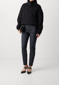 Svart oversized polo med tre knappar och ribbad krage, kombinerad med marinblå skräddarsydda byxor och svarta spetsiga ballerina-skor med guldfärgade detaljer.