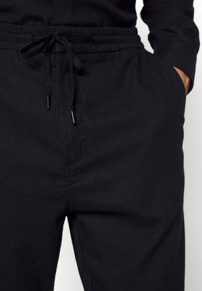 Calças de moletão pretas com cintura elástica e cordão, bolsos laterais e uma textura suave. O tecido parece durável e confortável.