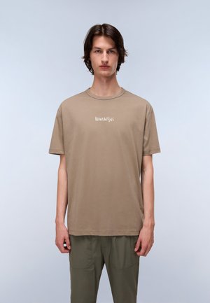 Brown cotton t-shirt featuring a crew neck, short sleeves, and a white logo print on the chest, paired with olive green pants.