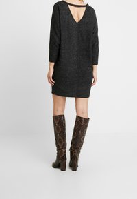 Robe en mélange de laine grise avec des manches trois-quarts, décolleté en V au dos et coupe décontractée. Assortie à des bottes marron à motif serpent montant jusqu'aux genoux.