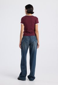 Maroon lyhythihainen t-paita valkoisilla yksityiskohdilla, yhdistettynä löysiin tummansinihin farkkuihin, joissa on suora leikkaus ja takataskut.