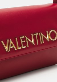 Borsa a mano in pelle rossa con una texture liscia, logo metallici dorato "VALENTINO" e un design strutturato.