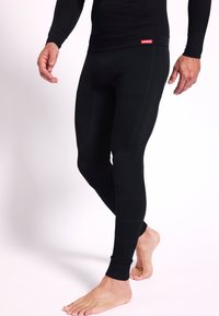 Leggings térmicos negros con tejido texturizado y diseño ajustado. Presentan un sutil detalle de marca a lo largo del costado y puños acanalados en los tobillos.