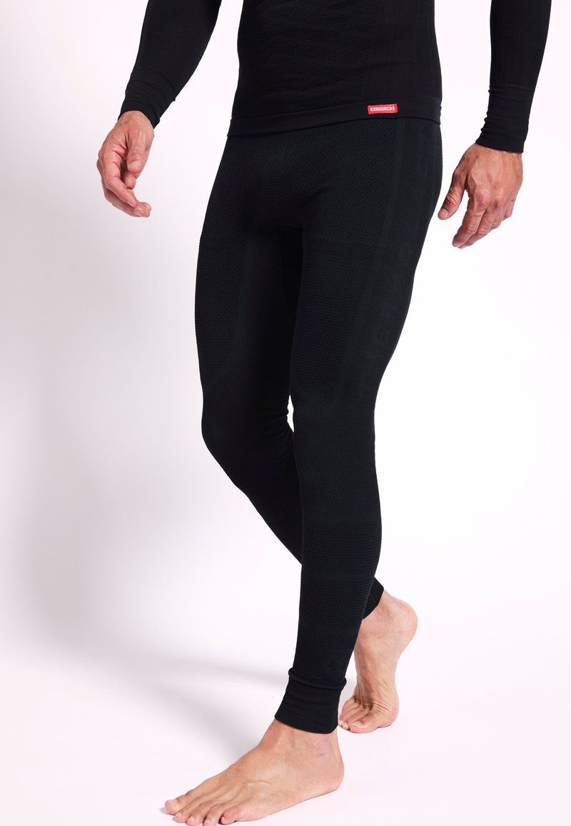 Leggings térmicos negros con tejido texturizado y diseño ajustado. Presentan un sutil detalle de marca a lo largo del costado y puños acanalados en los tobillos.
