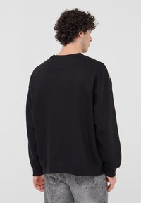 Felpa nera oversize in morbido tessuto, con scollatura a girocollo e spalle scese, caratterizzata da un design posteriore senza cuciture.