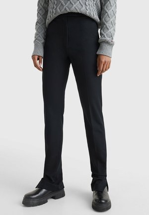 Persona que lleva pantalones negros de corte recto, botines negros gruesos y un suéter gris de punto de trenzas con mangas largas.