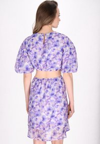 Violet kukkaistettu mekko puffi-hihoilla ja lyhyellä yläosalla. Pehmeä, virtaava kangas, jossa avonainen selkä ja joustava vyötärö.