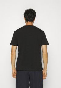 Czarny t-shirt z krótkim rękawem, okrągłym dekoltem i luźnym krojem, wykonany z miękkiej bawełny, zaprezentowany od tyłu.
