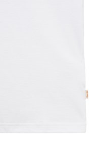 Vue recadrée d'un tissu blanc uni avec une petite étiquette tissée beige sur le bord droit, près de l'ourlet inférieur.