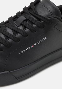 Baskets en cuir noir à finition texturée, bout arrondi, lacets plats noirs et logo "TOMMY HILFIGER" blanc sur le côté. Semelle en caoutchouc.