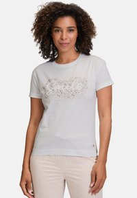 Hvid kortærmet t-shirt med et glitrende tekstdesign. Blødt stof, rund halsudskæring og opsmøgede ærmer. Kombineret med lyse bukser.