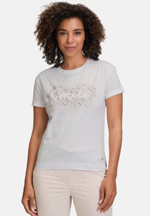 T-shirt blanc à manches courtes avec un design textuel pailleté. Tissu doux, col rond et manches à revers. Associé à un pantalon de couleur claire.