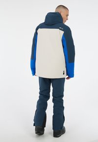 Schneejacke mit beigem Körper und blauen sowie navyfarbenen Ärmeln, Kapuze und Details. Das Material scheint strapazierfähig und hat eine lässige Passform.
