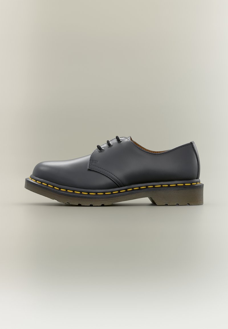Chaussure noire en cuir à lacets avec couture jaune autour de la semelle et une semelle extérieure en caoutchouc épaisse et translucide.