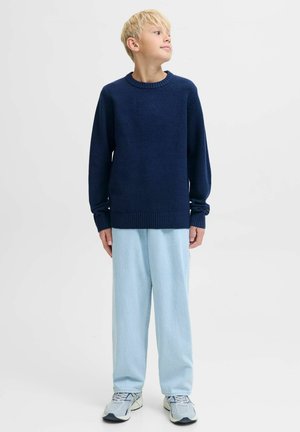 Un pull bleu marine avec un col rond et des poignets côtelés, associé à un pantalon large bleu clair et des baskets grises. Design épuré et minimaliste.