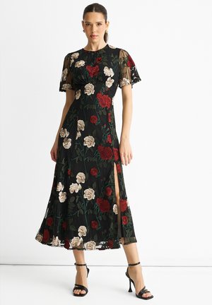 Black floral dress featuring embroidered roses in red and cream, sheer sleeves, a fitted bodice, and a side slit for added detail.