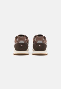 Scarpe da ginnastica marroni realizzate con una combinazione di materiali scamosciati e in pelle, con accenti grigi, un profilo basso e una suola in gomma beige chiaro.