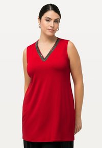 Červený bezrukávový tunikový top s výstřihem do V, zdobený černým dekorativním lemem kolem výstřihu. Měkká, hladká látka s volným střihem.