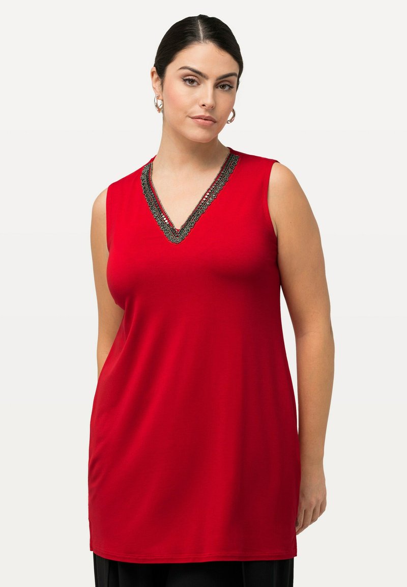Červený bezrukávový tunikový top s výstřihem do V, zdobený černým dekorativním lemem kolem výstřihu. Měkká, hladká látka s volným střihem.