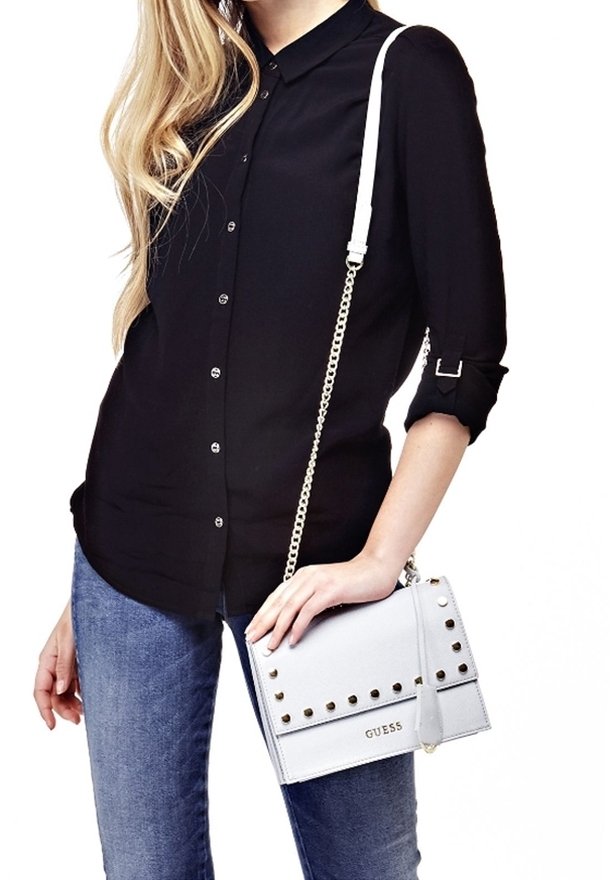 Svetle šedá kožená kabelka s zlatými hroty, řetízkem na rameno a klopovým uzavřením, s vyraženým názvem značky "GUESS" na přední straně.