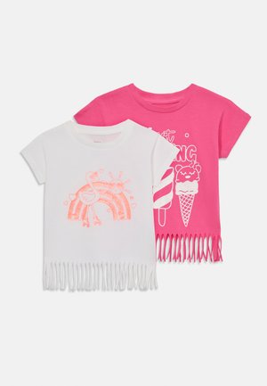 Δύο T-shirt: ένα λευκό με φούντες, που διαθέτει σχέδιο με ροζ φλαμίνγκο και ουράνιο τόξο; ένα ροζ με φούντες, που απεικονίζει γραφικά από παγωτό και γλυκά.