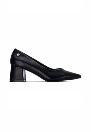 Zapato de mujer de piel negra con tacón bajo de bloque, punta afilada y pequeño logo metálico redondo cerca del talón.