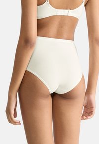 Mutande a vita alta di colore crema realizzate in tessuto morbido, con bordi senza cuciture e una consistenza liscia, dal design semplice e senza motivi visibili.