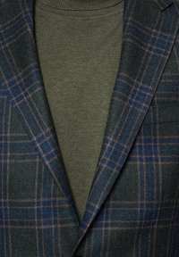 Marynarka w ciemnozieloną i granatową kratę z wełnianego materiału, z brązowymi akcentami, nałożona na dopasowany oliwkowy bawełniany golf.