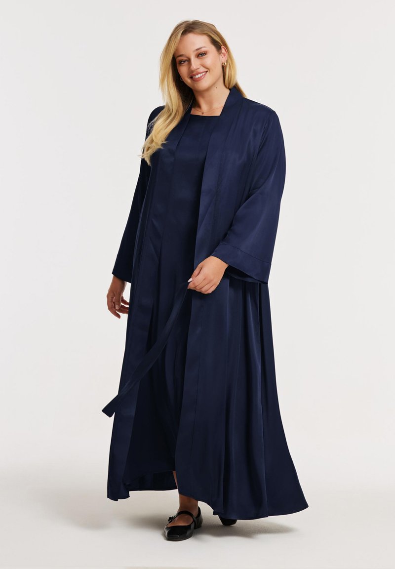 Marineblauwe satijnen maxi-jurk met lange mouwen en een bijpassende kimono. Zachte textuur, vloeiende silhouet en taillebanddetail.