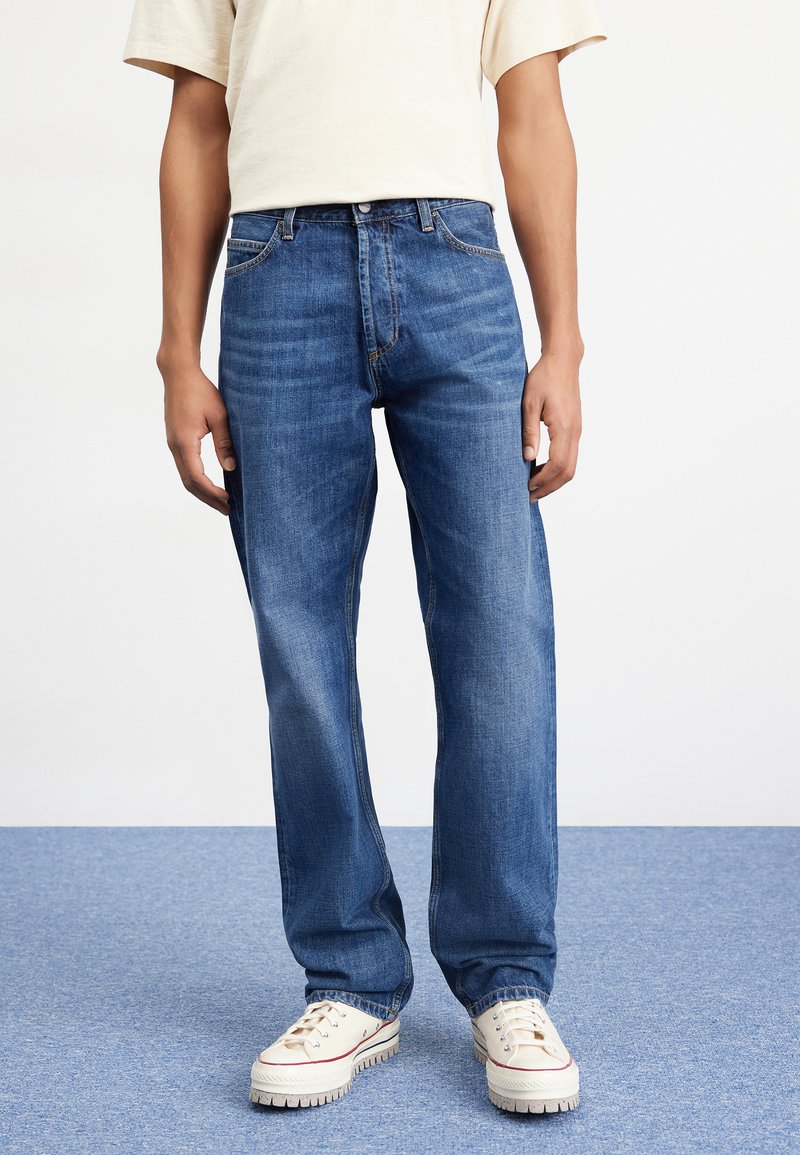 Blue denim jeans with a straight fit, featuring a classic five-pocket design and blue stitching. Worn with white sneakers.