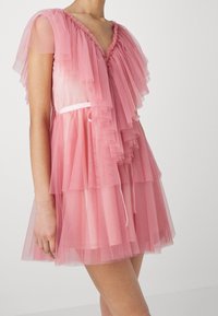 Robe en tulle rose avec des volants superposés, un décolleté en V, des manches courtes et une taille cintrée avec un délicat nœud en ruban.