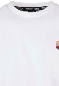 T-shirt en coton blanc avec un col rond et un imprimé graphique coloré sur le devant. Le col intérieur comporte un logo.