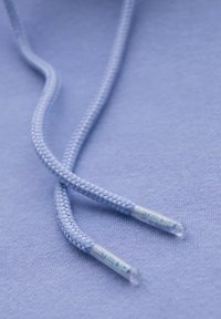 Cordon tressé bleu clair avec des embouts en plastique transparent, reposant sur un fond en tissu bleu clair assorti. Texture lisse.