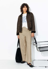 Veste en imprimé léopard marron, t-shirt graphique blanc, pantalon large beige, sac tote noir et chaussures noires à enfiler avec des pois.