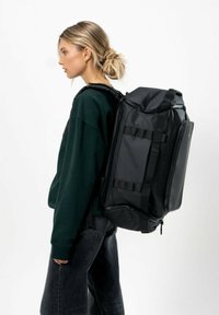 Zaino nero realizzato in materiale resistente, dotato di più cinghie, una tasca anteriore con zip e una forma rettangolare elegante.